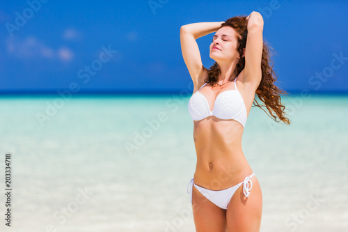 Young woman in white bikini standing on the ocean beach