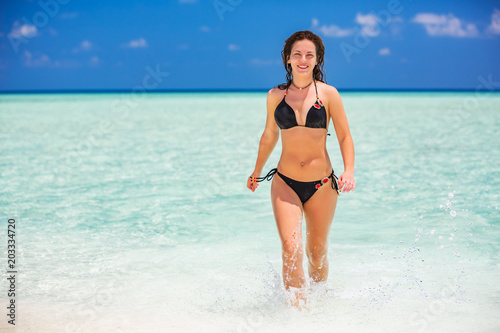 Attractive young woman enjoys Maldivian beach running in the ocean water