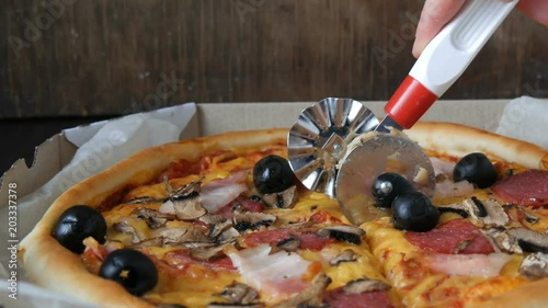 Hand cut a piece of a Big Italian pizza with black olives, bacon, salami and cheese close up photo