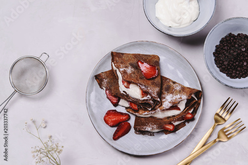 Homemade chocolate crepes with strawberry and cream on grey concrete background. Delicious breakfast. Selective focus