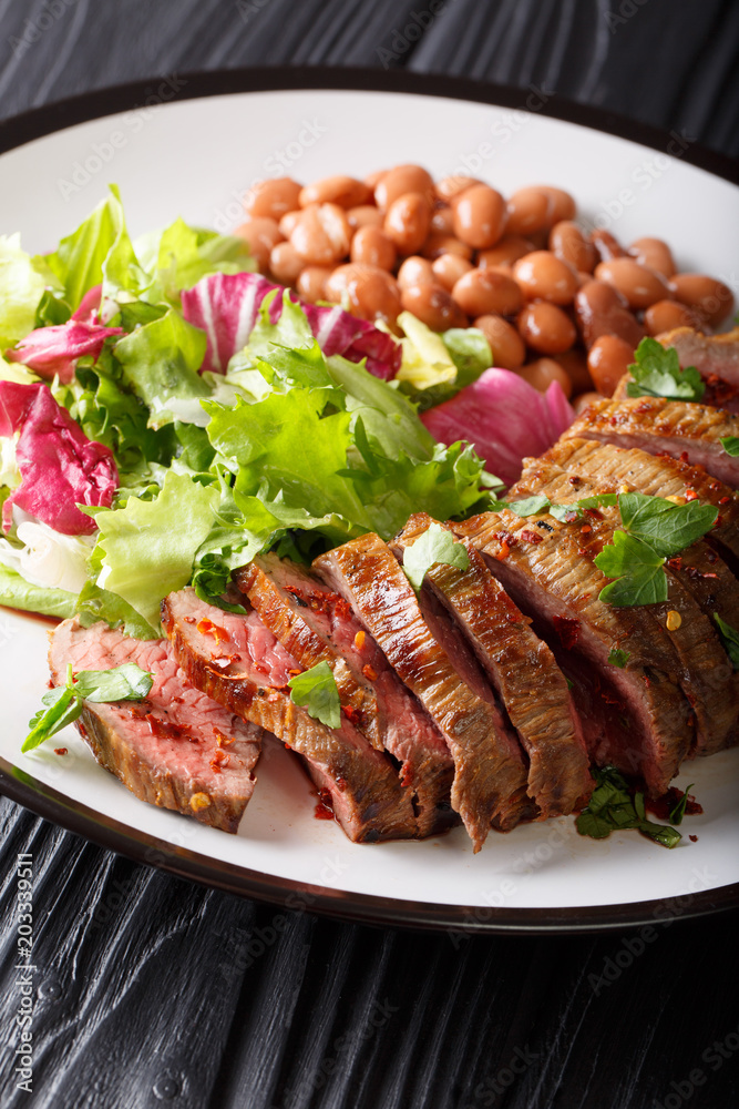 Grilled Carne Asada steak with salad and beans close-up on a plate. vertical Grilled Carne Asada steak with salad and beans close-up on a plate. vertical