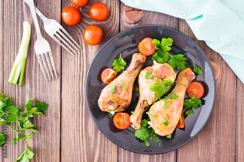 Baked chicken legs in spices with tomatoes and greens in a plate on a wooden table. Top view