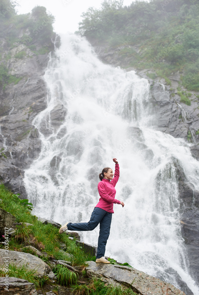 Portrait of female model in nature landscape with tourist attraction waterfall Balea in Fagarash mountains. Rocky waterfall in the mountains. The place of Carpathians Romania. Portrait of female model in nature landscape with tourist attraction waterfall Balea in Fagarash mountains. Rocky waterfall in the mountains. The place of Carpathians Romania.