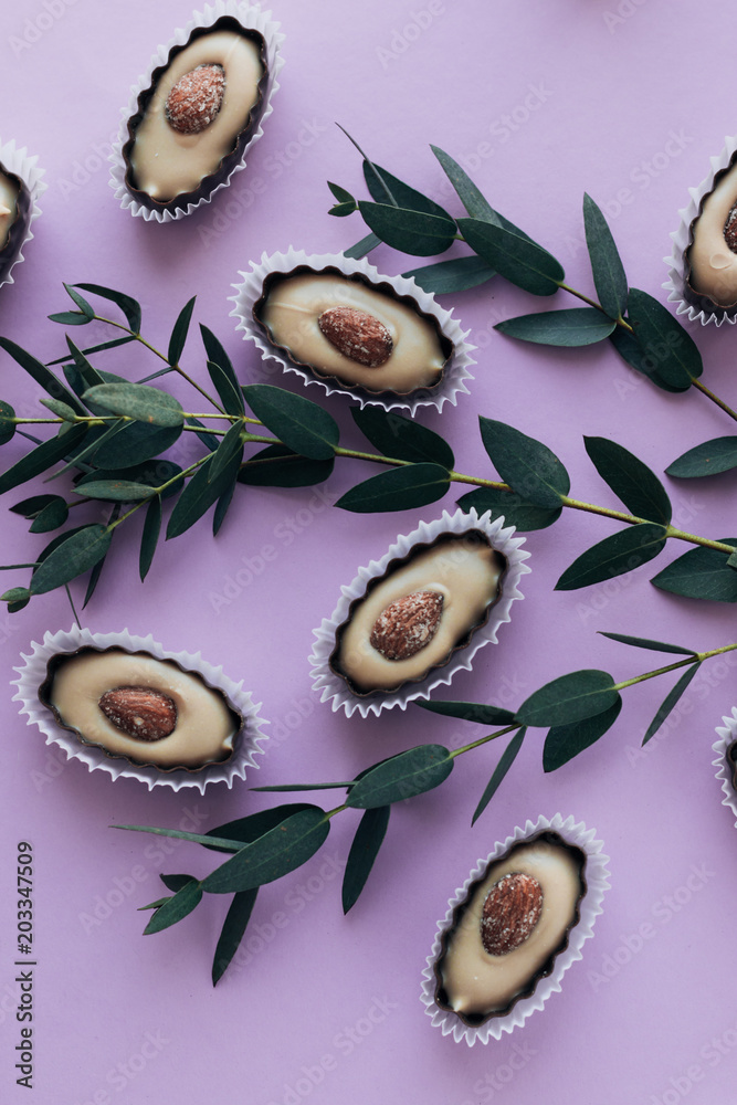 Composition of delicious praline sweets with almonds and green twigs on purple background Composition of delicious praline sweets with almonds and green twigs on purple background