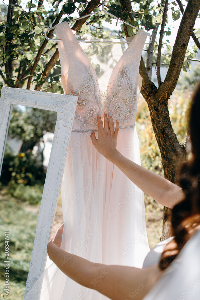 Naklejka premium The bride is touching her wedding dress with her hand standing in the garden. Bride's morning in the garden. Fine art wedding. Portrait of a young beautiful sexy tender bride. Closeup view