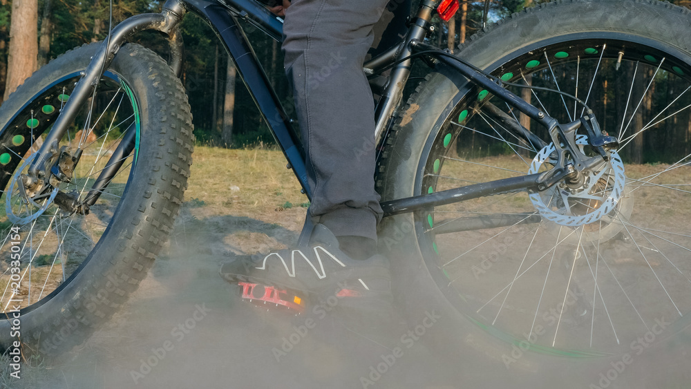 Fat bike also called fatbike or fat-tire bike in summer riding in the forest. The guy rides a bicycle on the forest soil. It goes into a controlled skid by the rear wheel. The dust and sand fly into Fat bike also called fatbike or fat-tire bike in summer riding in the forest. The guy rides a bicycle on the forest soil. It goes into a controlled skid by the rear wheel. The dust and sand fly into