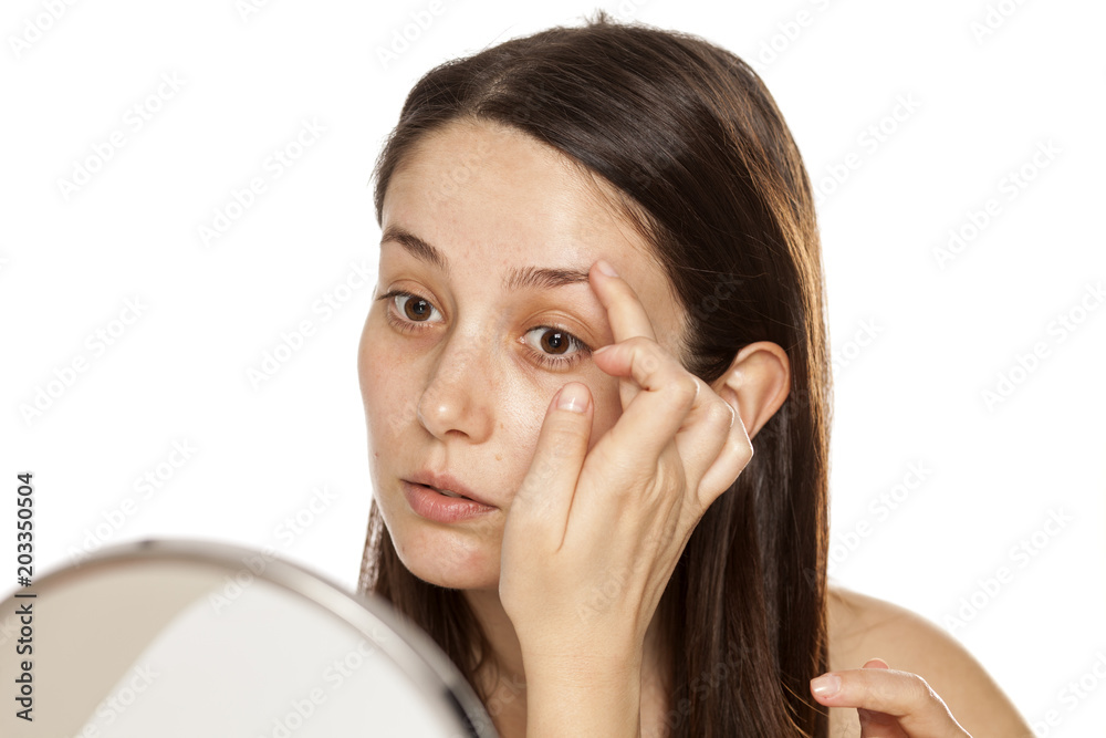Beautiful young woman touch her eyebrow in mirror on white background Beautiful young woman touch her eyebrow in mirror on white background