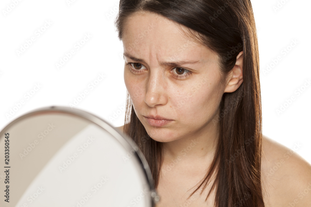 Unsatisfied young woman looking at her self in mirror on white background Unsatisfied young woman looking at her self in mirror on white background