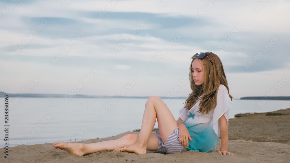 One beautiful teenage girl with brown hair outside on a beautiful summer day. The woman is sitting on the beach. The sun was gone in the sunset. One beautiful teenage girl with brown hair outside on a beautiful summer day. The woman is sitting on the beach. The sun was gone in the sunset.
