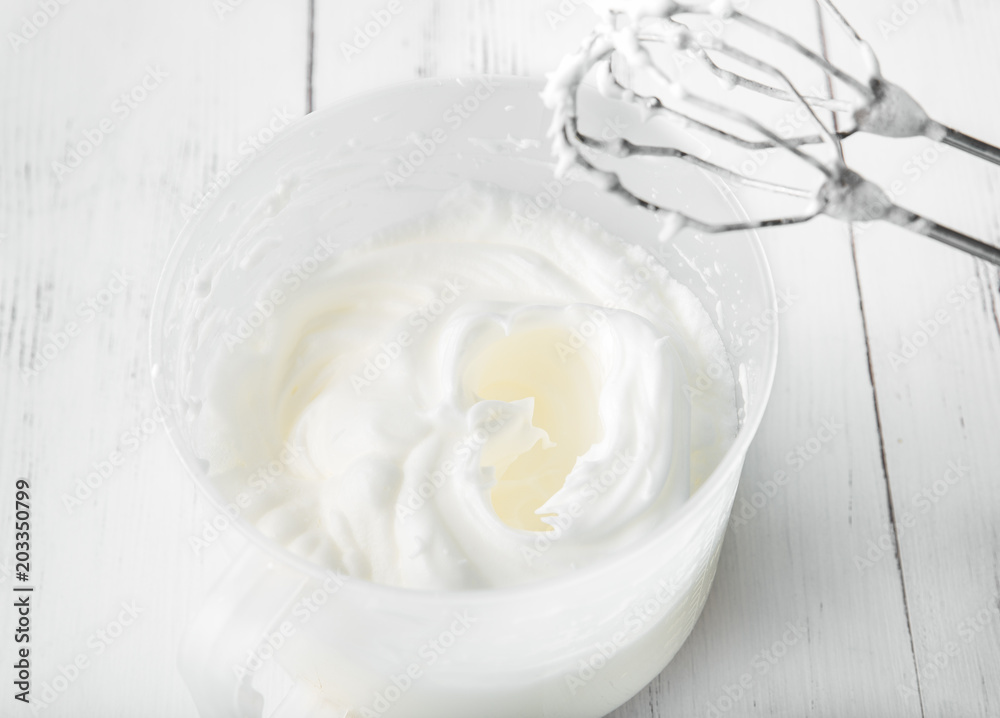 Cooking in the kitchen: whipped whites in a whisk can on a white wooden background, top view Cooking in the kitchen: whipped whites in a whisk can on a white wooden background, top view