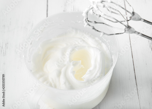 Cooking in the kitchen: whipped whites in a whisk can on a white wooden background, top view