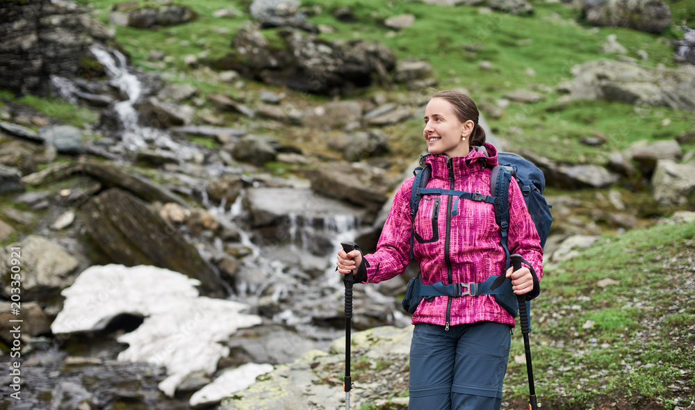 Close-up portrait of happy young woman with backpack and trekking sticks in the mountains. Concept healthy and active lifestyle.
