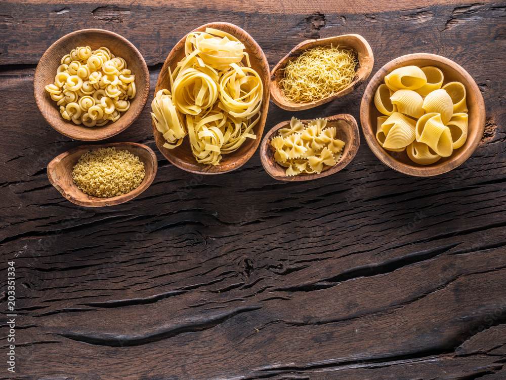 Different pasta types in wooden bowls on the table. Top view.