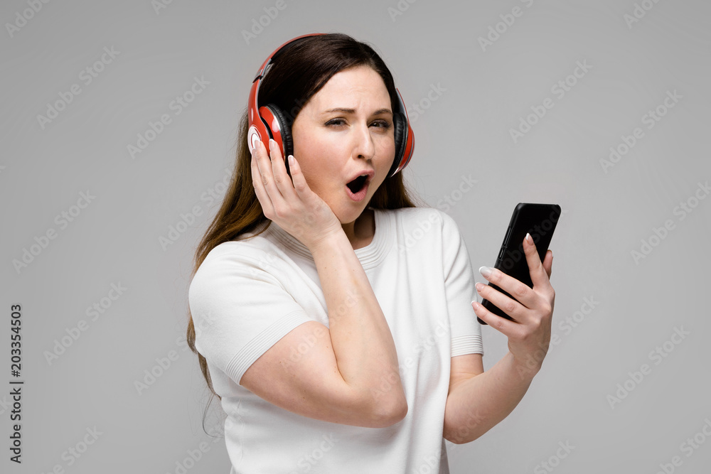 Portrait of emotional beautiful happy plus size model in headphones looking in camera holding mobile phone listening to music Portrait of emotional beautiful happy plus size model in headphones looking in camera holding mobile phone listening to music