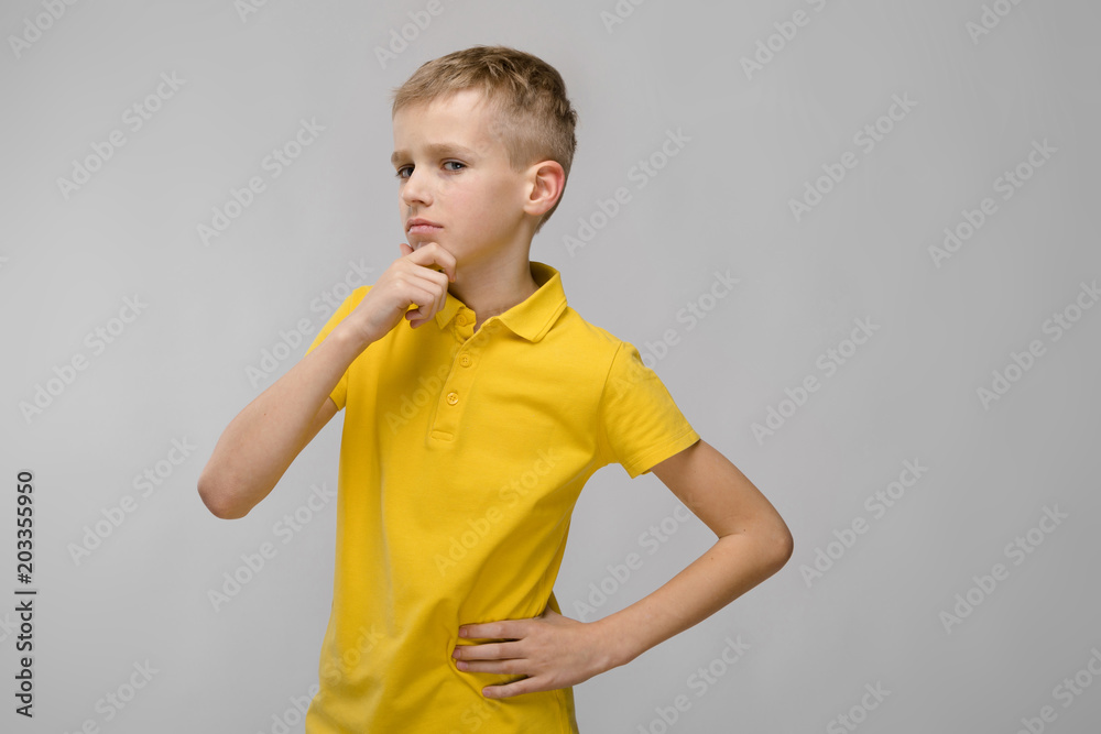 Portrait of cute little blonde caucasian boy in yellow t-shirt unsure puzzled on gray background Portrait of cute little blonde caucasian boy in yellow t-shirt unsure puzzled on gray background