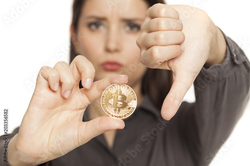 unhappy woman holding a golden bitcoin and showing thumbs down