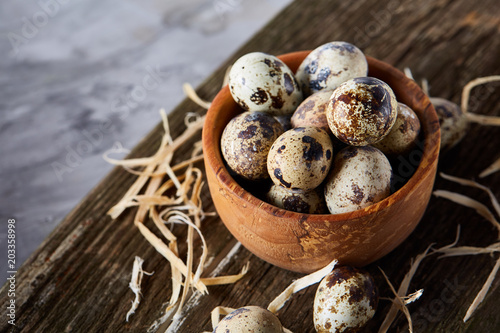 Wooden bowl filled with quail eggs on wooden board over white background, close-up, selective focus.