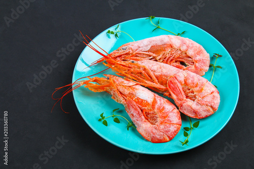 Large royal raw frozen prawns on a blue plate with thyme and basil on a concrete table. Red shrimps. Top view.