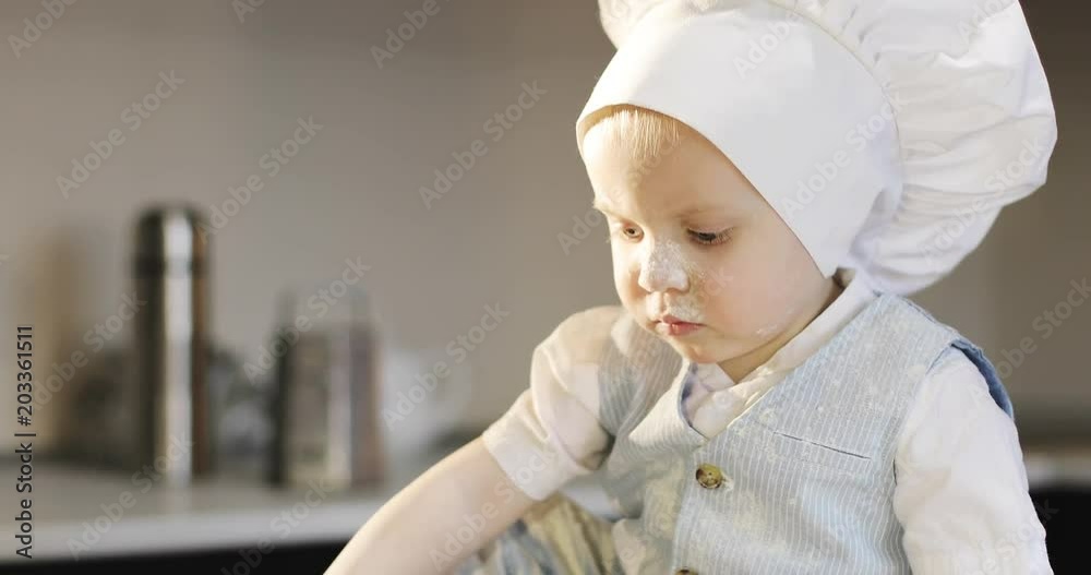 A sweet small chef cook in a white culinary cap mixes the flour with a metal spoon. A sweet small chef cook in a white culinary cap mixes the flour with a metal spoon.