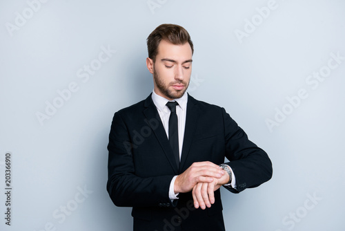 Portrait of confident smart clever fashionable successful wealthy wearing black formal outfit and trendy white shirt lawyer, he is checking time om his silver wristwatch, isolated om gray background