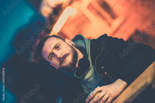 A retro style photo of a young hipster man sitting at the table and drinking wine at night in a urban environment.