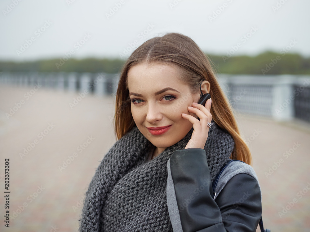 A stylish blonde in a fashionable urban style speaks on the phone, on the headset in a park on the river bank. The concept of spring mood A stylish blonde in a fashionable urban style speaks on the phone, on the headset in a park on the river bank. The concept of spring mood