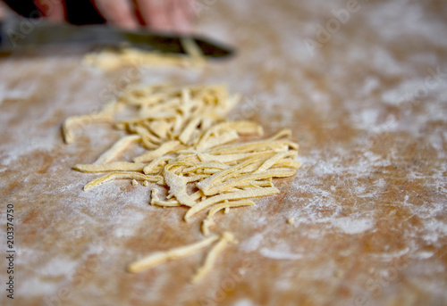 Women's hands cutting dough for homemade noodles on wooden cutting board. Close up, isometric.