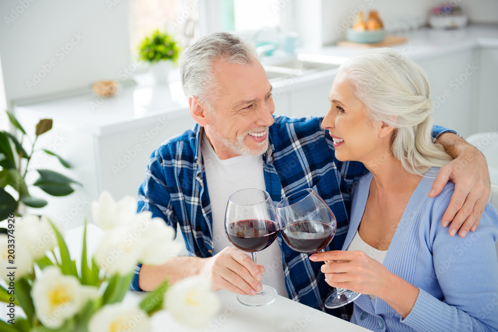 Lovely cheerful stylish attractive romantic couple sitting in the kitchen clinking glasses with red wine looking at each other enjoying time together, handsome man hugging his beautiful lover Lovely cheerful stylish attractive romantic couple sitting in the kitchen clinking glasses with red wine looking at each other enjoying time together, handsome man hugging his beautiful lover