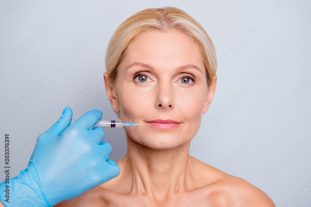 Portrait of calm serious aged woman with wrinkle making augmentation injection in lips in clinic salon isolated on grey background enhancement concept Portrait of calm serious aged woman with wrinkle making augmentation injection in lips in clinic salon isolated on grey background enhancement concept