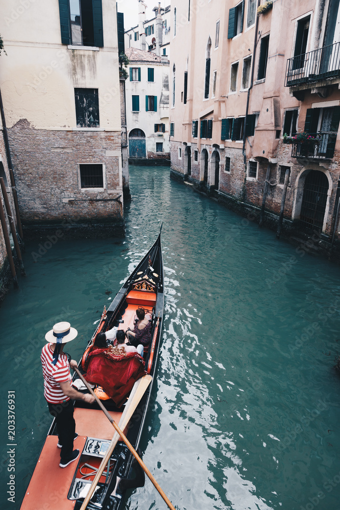 Gondolier with gondola through green canal waters of Venice Italy