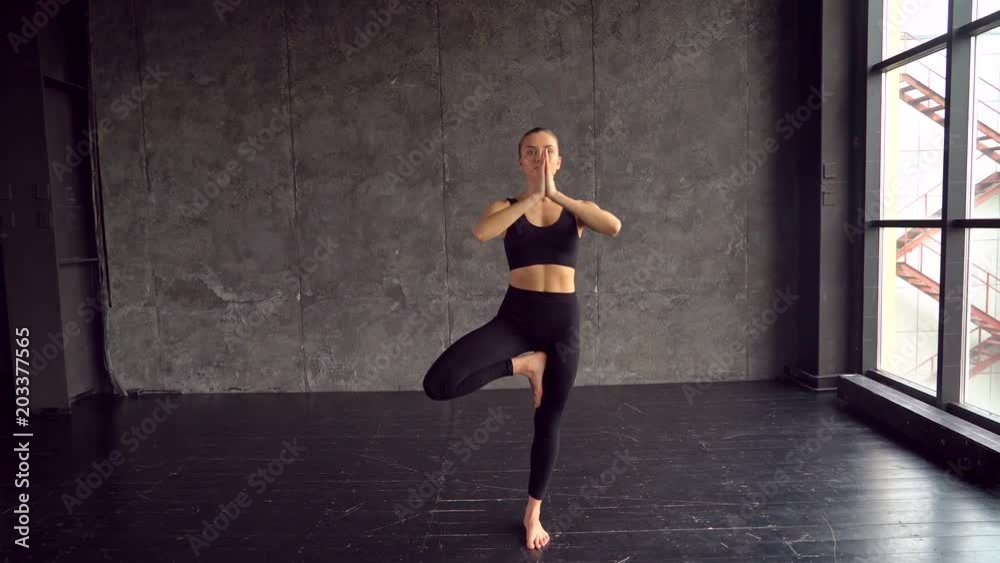 Caucasian young girl doing yoga exercise. Athletic woman yoga training. Young slim sporty girl holds her hands in Namaste posture Woman do yoga indoors. 20s. Yoga woman. Tree pose. 4 k Caucasian young girl doing yoga exercise. Athletic woman yoga training. Young slim sporty girl holds her hands in Namaste posture Woman do yoga indoors. 20s. Yoga woman. Tree pose. 4 k
