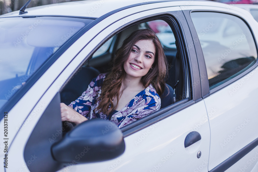 Young woman driving a car in the city. Portrait of a beautiful woman in a car, looking out of the window and smiling. Travel and vacations concepts