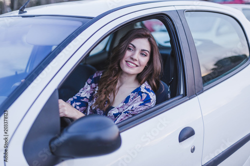 Young woman driving a car in the city. Portrait of a beautiful woman in a car, looking out of the window and smiling. Travel and vacations concepts © Eva