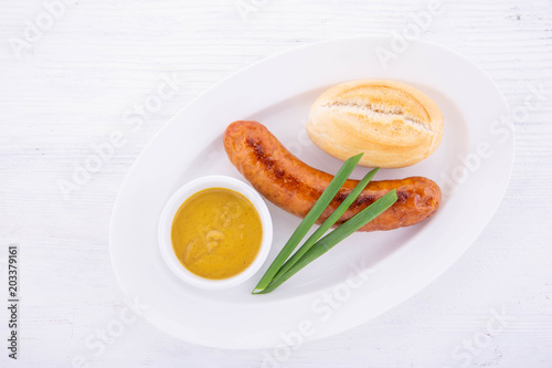 Fried sausage from beef on a white plate and a white wooden background, with white loaf, green onions and mustard