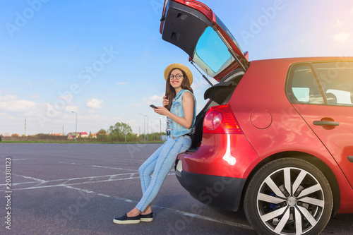 Young woman traveler sitting on hatchback car with outdoor sunny  background 
 photo