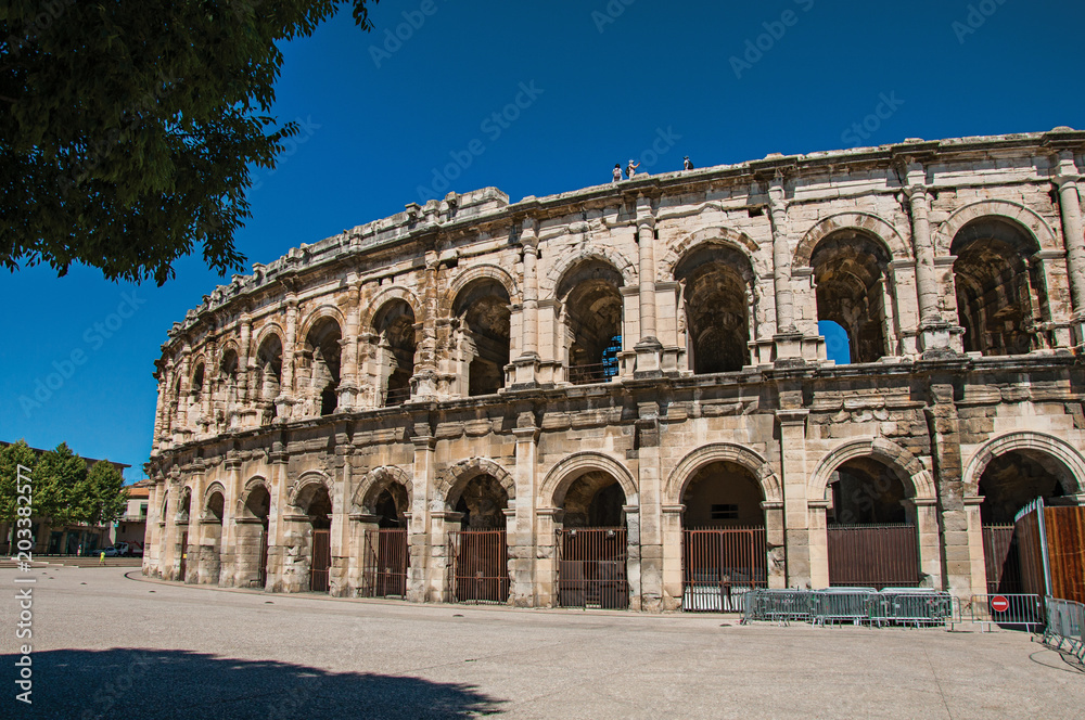 Partial view of the exterior of the Arena of Nimes, an amphitheater of the Roman Era, with sunny blue sky. Located in the Gard department, Occitanie region in southern France