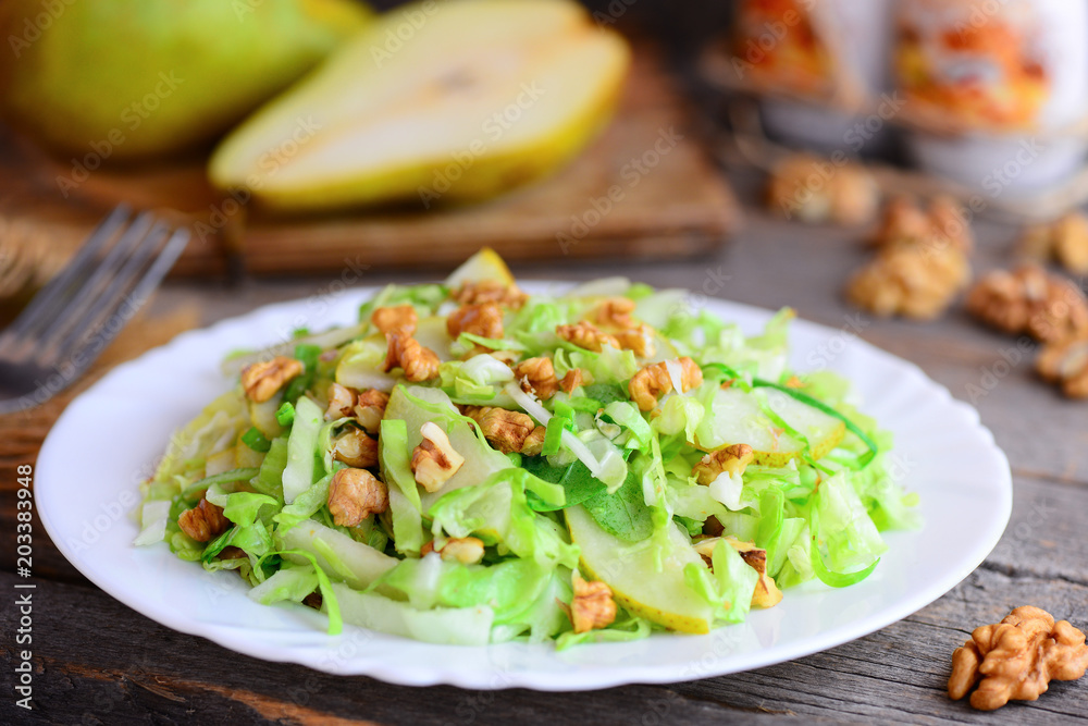 Pear cabbage slaw salad. Homemade salad with fresh pear, cabbage and walnuts on a white plate and on rustic wooden background. Comfort food lunch recipe. Cooking light diet. Closeup Pear cabbage slaw salad. Homemade salad with fresh pear, cabbage and walnuts on a white plate and on rustic wooden background. Comfort food lunch recipe. Cooking light diet. Closeup