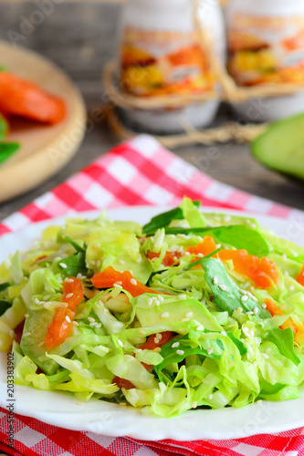 Easy avocado cabbage coleslaw. Diet cabbage salad with fresh avocado, dried apricots, arugula and sesame on a plate and on a wooden table. Healthy comfort food for vegetarians and vegans. Closeup