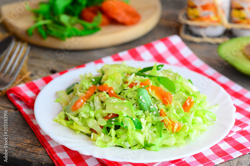 Cabbage and avocado slaw recipe. Easy cabbage salad with fresh avocado, dried apricots, arugula and sesame on a plate and on a wooden table. Healthy vegetarian comfort food. Closeup 