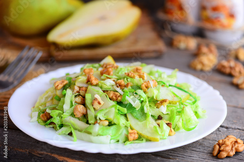 Pear cabbage slaw salad. Homemade salad with fresh pear, cabbage and walnuts on a white plate and on rustic wooden background. Comfort food lunch recipe. Cooking light diet. Closeup