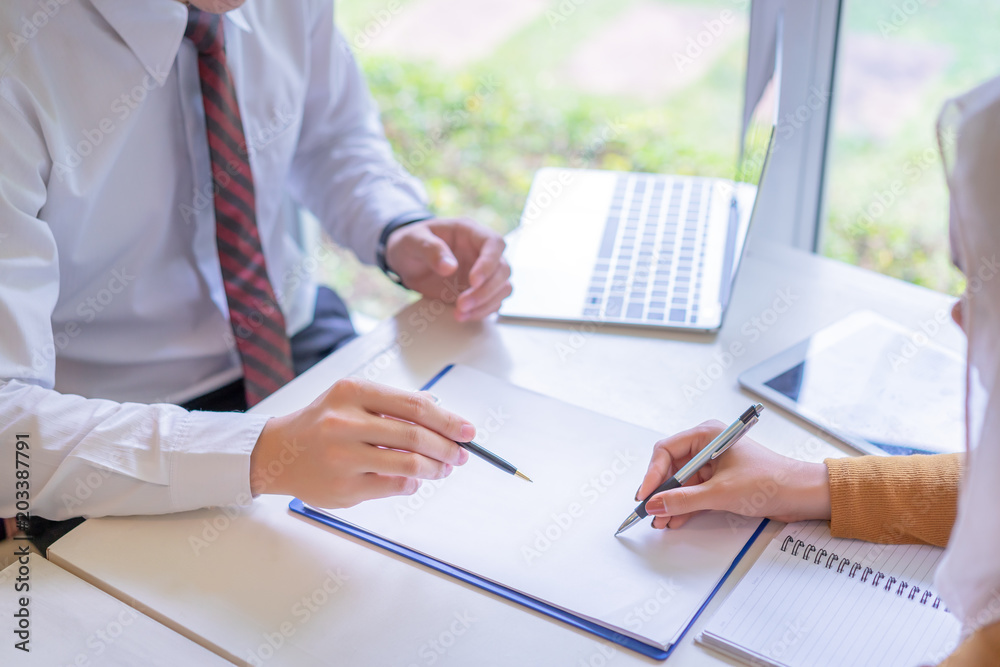 Two business point a pen to each other above blank paper at meeting or negotiation in the office.