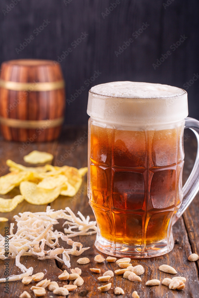 Fototapeta premium A mug of dark beer with peanut, dried squids and chips on a dark wooden background