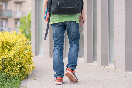 Teen boy 14 years old with backpack on the first or last school day. Excited to be back to school after vacation - outdoor back view. photo