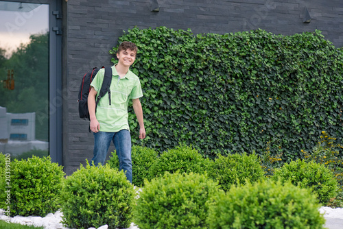 Outdoor portrait of happy teen boy 14 years old with backpack on the first or last school day. Excited to be back to school after vacation.