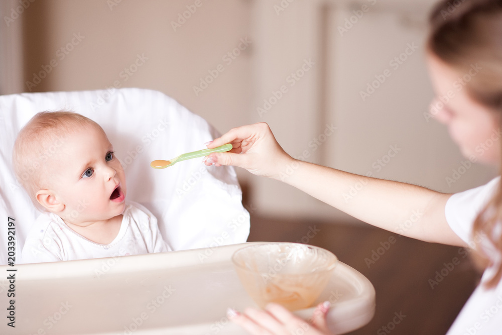 Young mother feeding baby with smashed fruits in room. Healthy eating. Young mother feeding baby with smashed fruits in room. Healthy eating.