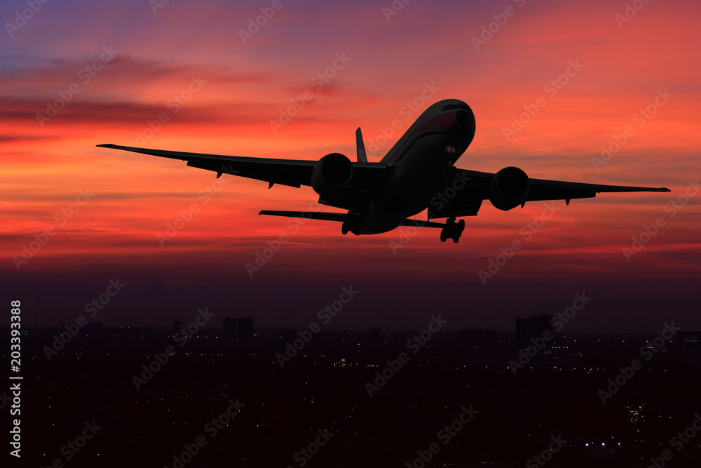 Commercial airplane flying over the night scene city on beautiful sunset background