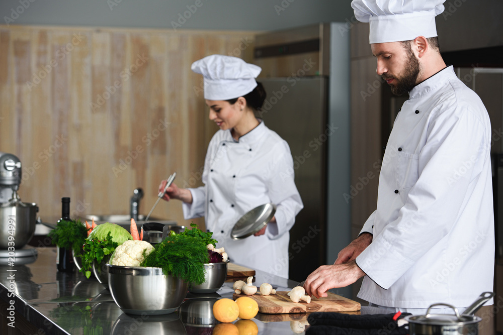 Professional chefs busy cooking by kitchen table Professional chefs busy cooking by kitchen table