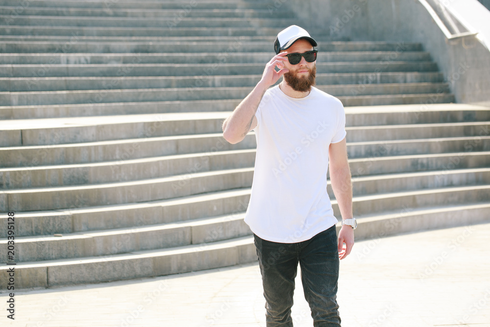 Hipster handsome male model with beard wearing white blank t-shirt and a baseball cap with space for your logo or design in casual urban style Hipster handsome male model with beard wearing white blank t-shirt and a baseball cap with space for your logo or design in casual urban style