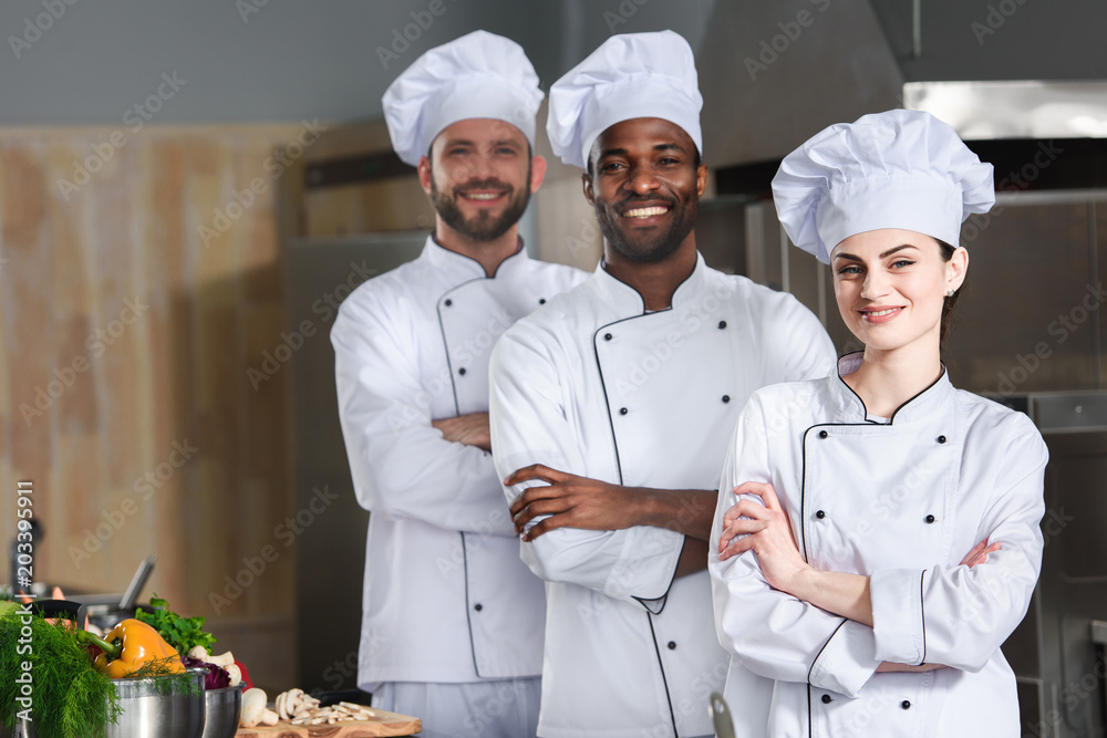 Multiracial chefs team posing with folded arms on kitchen