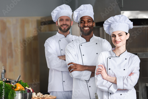 Multiracial chefs team posing with folded arms on kitchen photo